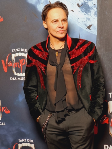 Rob Fowler trägt bei der Premiere von Tanz der Vampire 2023 in Hamburg ein Outfit aus schwarzem Samt und roten Strasssteinen von Christian Moore.